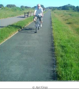 Older man riding a bicycle along a rural, paved bike path